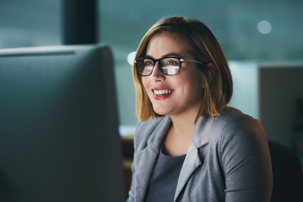 Woman with glasses working in the dark at a desktop computer